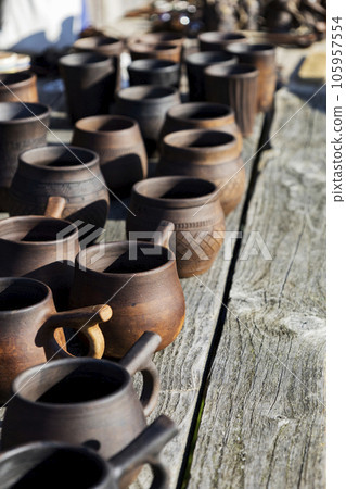 Many dark-colored clay pots stand on the table in pottery workshops. Sale of clay products. 105957554
