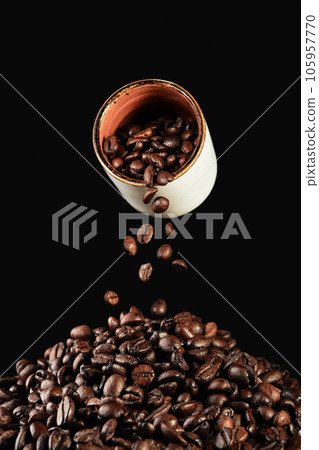 Falling coffee beans from a white cup and freshly roasted coffee beans on the table, vertical frame on a black background 105957770