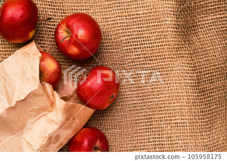 Ripe, juicy red apples float out of a paper bag on a background of coarse burlap. Top view flat lay with copy space. First summer harvest 105958175