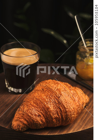 Coffee, croissant and jam on a wooden table. French breakfast in a cafe. Vertical shot, selective focus on a croissant 105958184