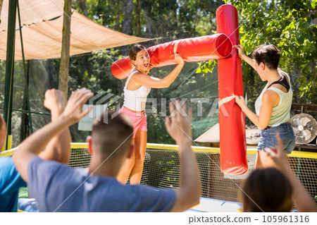 Young women having funny wrestling by inflatable logs in outdoor amusement playground 105961316