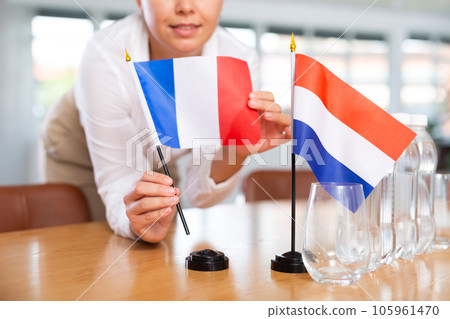 Young woman puts flags of France and Netherlands on table in office Young woman puts flags of France and Netherlands on table in office 105961470