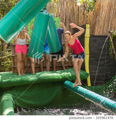 Cheerful woman trying to walk on inflatable log above pool of water Cheerful woman trying to walk on inflatable log above pool of water 105961476