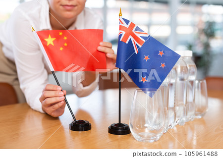 Preparing for business negotiations - woman sets small flags of countries of China and Australia on table 105961488