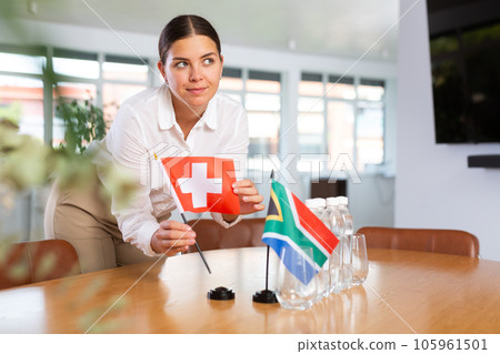 Positive young woman putting little flag of Switzerland on table next to the flag of South Africa 105961501