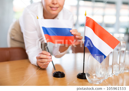 Young woman puts flags of Russia and Netherlands on table in office 105961533