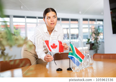 Positive young woman putting little flag of Canada on table next to the flag of South Africa Positive young woman putting little flag of Canada on table next to the flag of South Africa 105961536