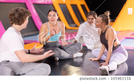 Group of enthusiastic young people sitting on trampoline and discussing upcoming jumping workout in entertainment center Group of enthusiastic young people sitting on trampoline and discussing upcoming jumping workout in entertainment center 105961538