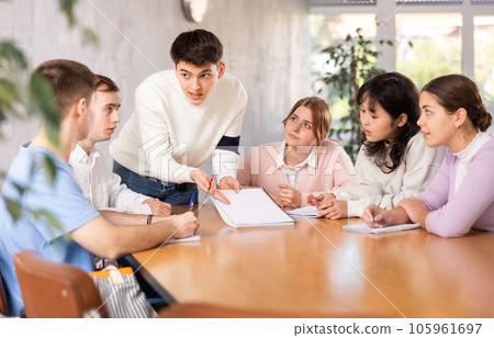 Young teacher discussing his notes with students around the table 105961697