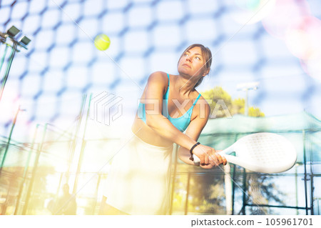 Athletic woman plays padel outdoor. View through tennis net Athletic woman plays padel outdoor. View through tennis net 105961701