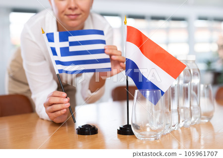 Employee of delegation prepares negotiating table - sets up flag of Netherlands and Greece 105961707
