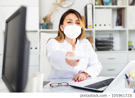 Woman doctor in medical mask is giving recipe to client Woman doctor in medical mask is giving recipe to client 105961728