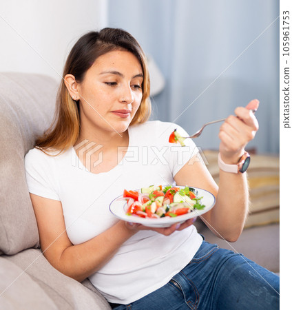 Peruvian housewoman eating vegetable salad on sofa at home 105961753