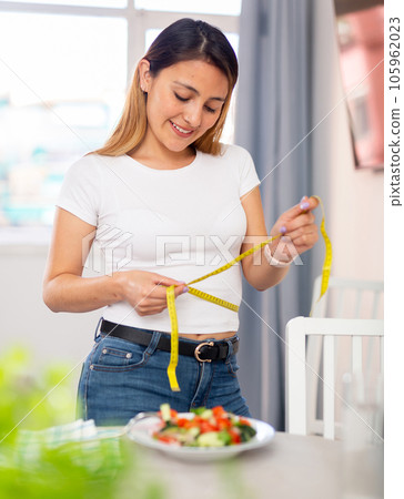 Colombian housewife measures waist before eating vegetable salad Colombian housewife measures waist before eating vegetable salad 105962023