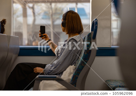 Woman tourist in headphones making photo on phone while traveling in public transport near window 105962096