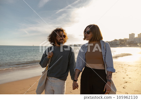 Smiling romantic couple in love is walk holding hands across the beach on sunset Smiling romantic couple in love is walk holding hands across the beach on sunset 105962110
