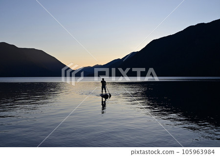 Silhouetted male paddleboarder on Lake Crescent in Olympic National Park. Silhouetted male paddleboarder on Lake Crescent in Olympic National Park. 105963984