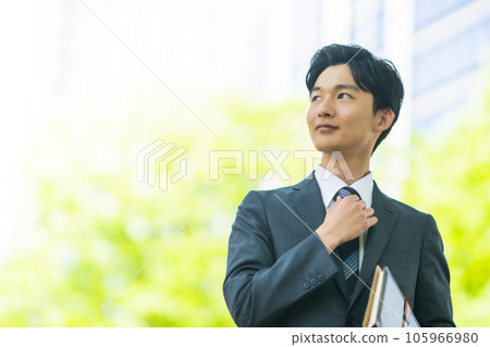 A young businessman walking around in a suit in the fresh green 105966980