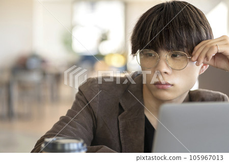 一個戴眼鏡的年輕人在咖啡館用電腦 105967013