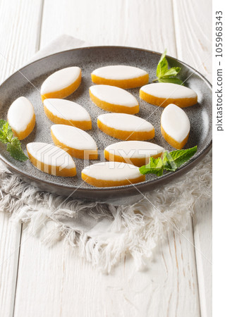 French candy Calissons consisting of pale yellow homogeneous paste of candied fruit melons and oranges and ground almonds topped with a thin layer of royal icing closeup on the plate. Vertical 105968343