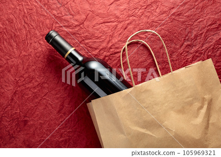 Paper shopping bag with a bottle of red wine on a textured red background. 105969321