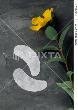Pair of thin patches using for isolating eyelshes and applying on lower eyelids lying on table near flower. 105969673