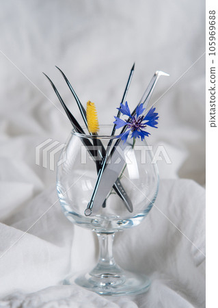 Various professional tools for eyelash extension procedure lying in wineglass with little cornflower on white sheet. Various professional tools for eyelash extension procedure lying in wineglass with little cornflower on white sheet. 105969688