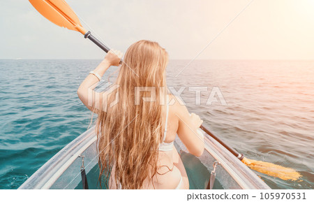 Woman in kayak back view. Happy young woman with long hair floating in transparent kayak on the crystal clear sea. Summer holiday vacation and cheerful female people relaxing having fun on the boat Woman in kayak back view. Happy young woman with long hair floating in transparent kayak on the crystal clear sea. Summer holiday vacation and cheerful female people relaxing having fun on the boat 105970531
