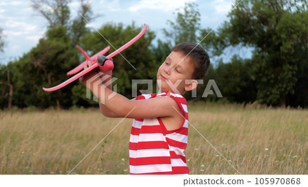 Adorable toddler boy walks with toy plane and imitates jet sounds on meadow with flowers. Little boy plays with toy runs in field grass. Joyful boy with toy plane enjoys summer vacation at countryside Adorable toddler boy walks with toy plane and imitates jet sounds on meadow with flowers. Little boy plays with toy runs in field grass. Joyful boy with toy plane enjoys summer vacation at countryside 105970868