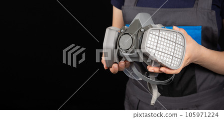 Respirator with dust and gas filters in the hands of a person on a black background. Respirator with dust and gas filters in the hands of a person on a black background. 105971224