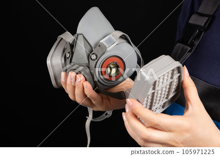 Respirator with dust and gas filters in the hands of a person on a black background. 105971225
