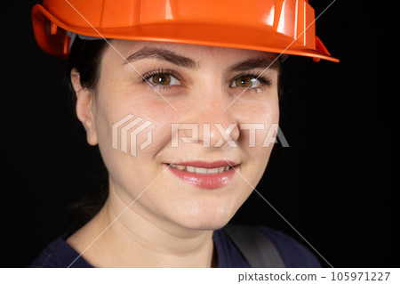 A female construction worker or engineer wearing a protective orange mask on a black background 105971227