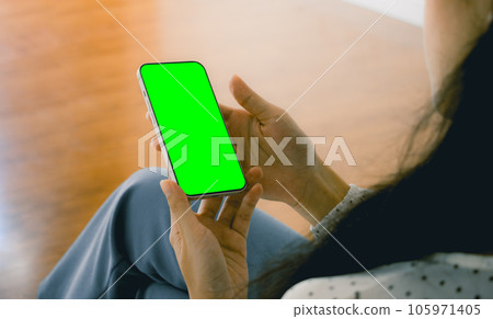 Mockup image, a woman holding black smartphone with blank green screen at home. Mockup image, a woman holding black smartphone with blank green screen at home. 105971405