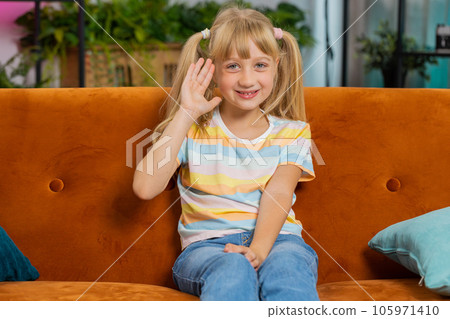 Child kid girl smiling friendly at camera, waving hands gesturing hello hi greeting at home on couch Child kid girl smiling friendly at camera, waving hands gesturing hello hi greeting at home on couch 105971410