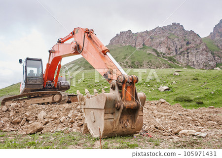 Excavator works in the highlands. Clears the consequences of a mudslide in the gorge of the mountains. repair and expansion of a road Excavator works in the highlands. Clears the consequences of a mudslide in the gorge of the mountains. repair and expansion of a road 105971431