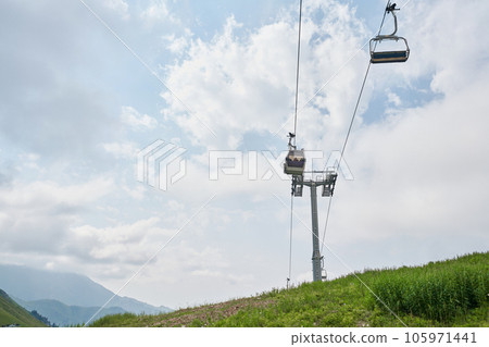 Empty chairlift in ski resort. Shot in summer with green grass and no snow. Cloudy weather. Empty chairlift in ski resort. Shot in summer with green grass and no snow. Cloudy weather. 105971441