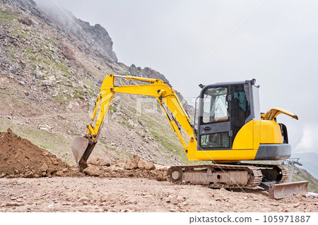 Excavator works in the highlands. Makes a trench for communications. water and electricity. in the gorge of the mountains. repair and expansion of a road Excavator works in the highlands. Makes a trench for communications. water and electricity. in the gorge of the mountains. repair and expansion of a road 105971887