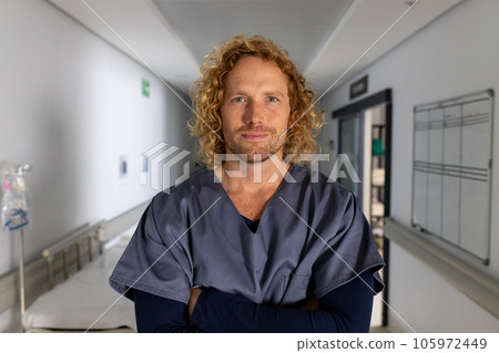 Portrait of happy caucasian male doctor wearing scrubs in corridor at hospital 105972449