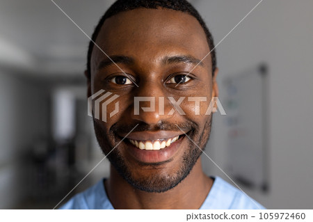 Portrait of happy african american male doctor wearing scrubs in corridor at hospital 105972460