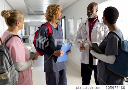 Senior african american male doctor talking to diverse trainee doctors in corridor at hospital Senior african american male doctor talking to diverse trainee doctors in corridor at hospital 105972488