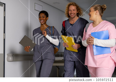 Happy diverse doctors wearing scrubs walking through corridor at hospital 105972511