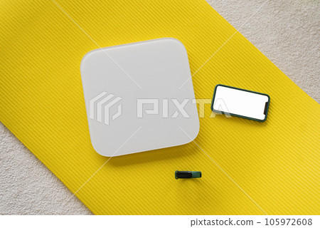 Scales, a smartphone and a fitness watch lie on a yellow yoga mat. View from above. Fitness trainer's weight control props 105972608