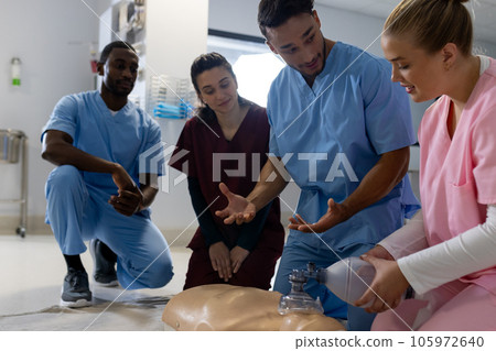 Biracial male doctor with diverse trainee doctors learning cpr on model at hospital 105972640