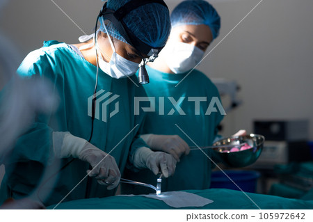 Diverse surgeons wearing surgical gowns operating on patient in operating theatre at hospital 105972642