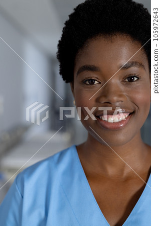 Portrait of happy african american female doctor wearing scrubs in corridor at hospital 105972643