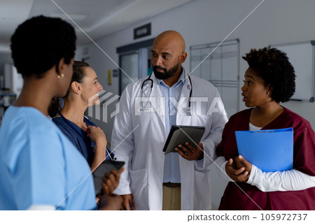 Diverse doctors using tablets and discussing work in corridor at hospital Diverse doctors using tablets and discussing work in corridor at hospital 105972737