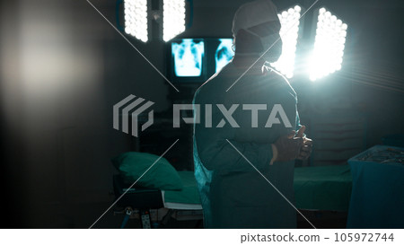 Biracial male surgeon wearing surgical gown and face mask in operating theatre at hospital Biracial male surgeon wearing surgical gown and face mask in operating theatre at hospital 105972744