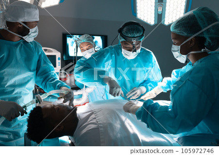 Diverse surgeons wearing surgical gowns operating on patient in operating theatre at hospital Diverse surgeons wearing surgical gowns operating on patient in operating theatre at hospital 105972746