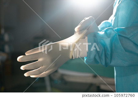 Midsection of biracial female surgeon wearing surgical gown and gloves in operating theatre Midsection of biracial female surgeon wearing surgical gown and gloves in operating theatre 105972760