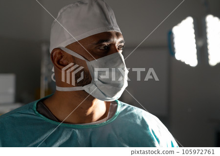 Biracial male surgeon wearing surgical gown and face mask in operating theatre at hospital Biracial male surgeon wearing surgical gown and face mask in operating theatre at hospital 105972761